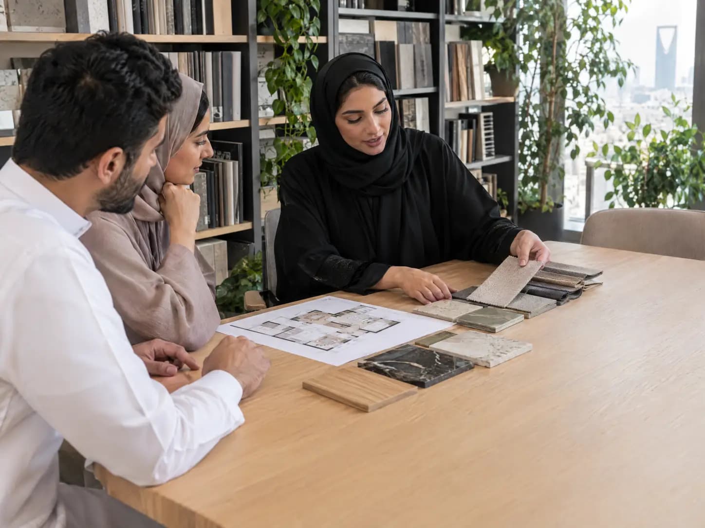 A designer showing material samples and a floor plan to a couple in a Riyadh studio